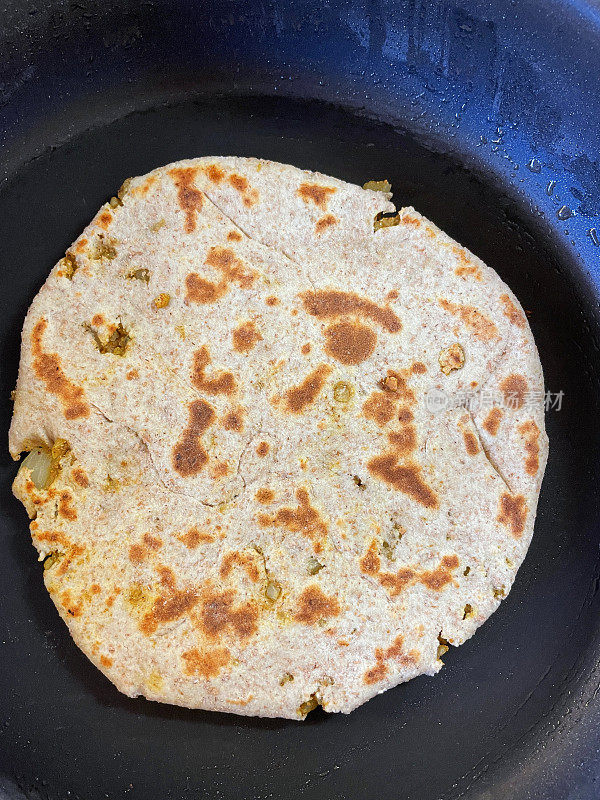 图片中的不粘锅里装着自制的gobi aloo paratha，塞满了香料土豆、花椰菜和洋葱的咸味面包，在平底锅里煎着，高架视野